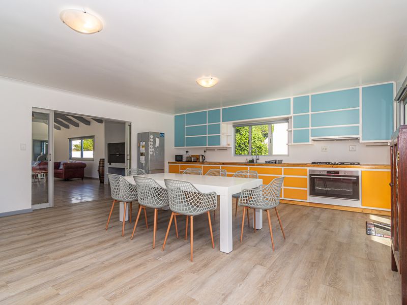 Open-plan kitchen and dining area featuring vibrant blue and orange cabinetry, integrated oven, gas hob, and modern laminate flooring with access to an adjacent room.