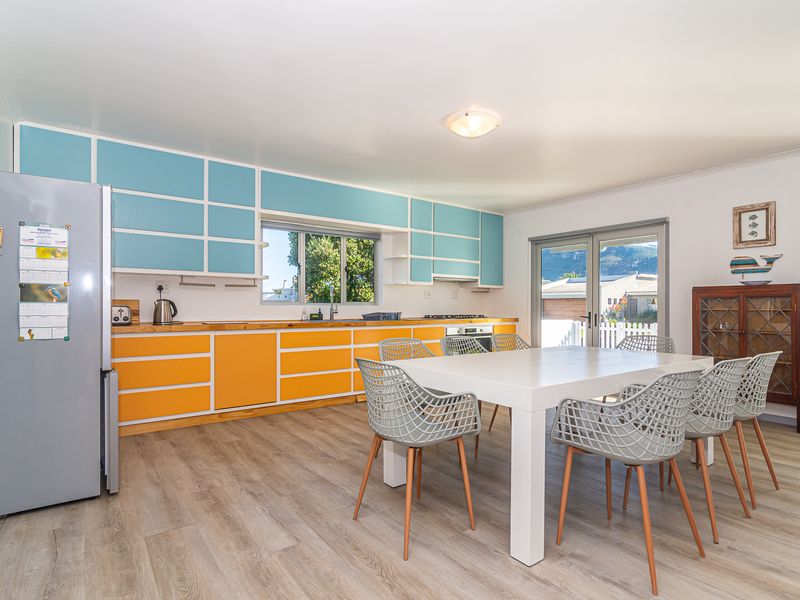 Open-plan kitchen and dining area featuring vibrant two-tone cabinetry, laminate flooring, and direct access to the exterior through sliding glass doors.