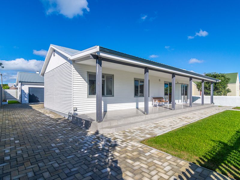 A well-maintained rear exterior view featuring a spacious covered patio, paved driveway, and neat garden area with a detached garage.