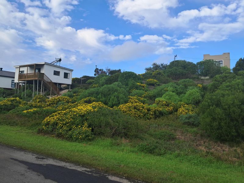 A view of a sloped residential plot featuring an elevated dwelling with a wooden staircase and solar water heating system.