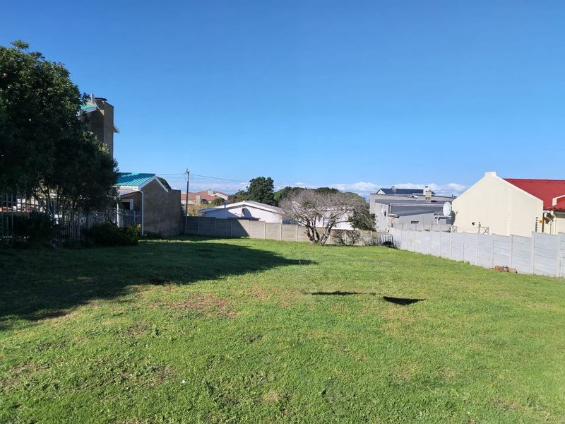 A level, grassed residential plot enclosed by precast concrete boundary walls, situated in a developed suburban neighborhood.