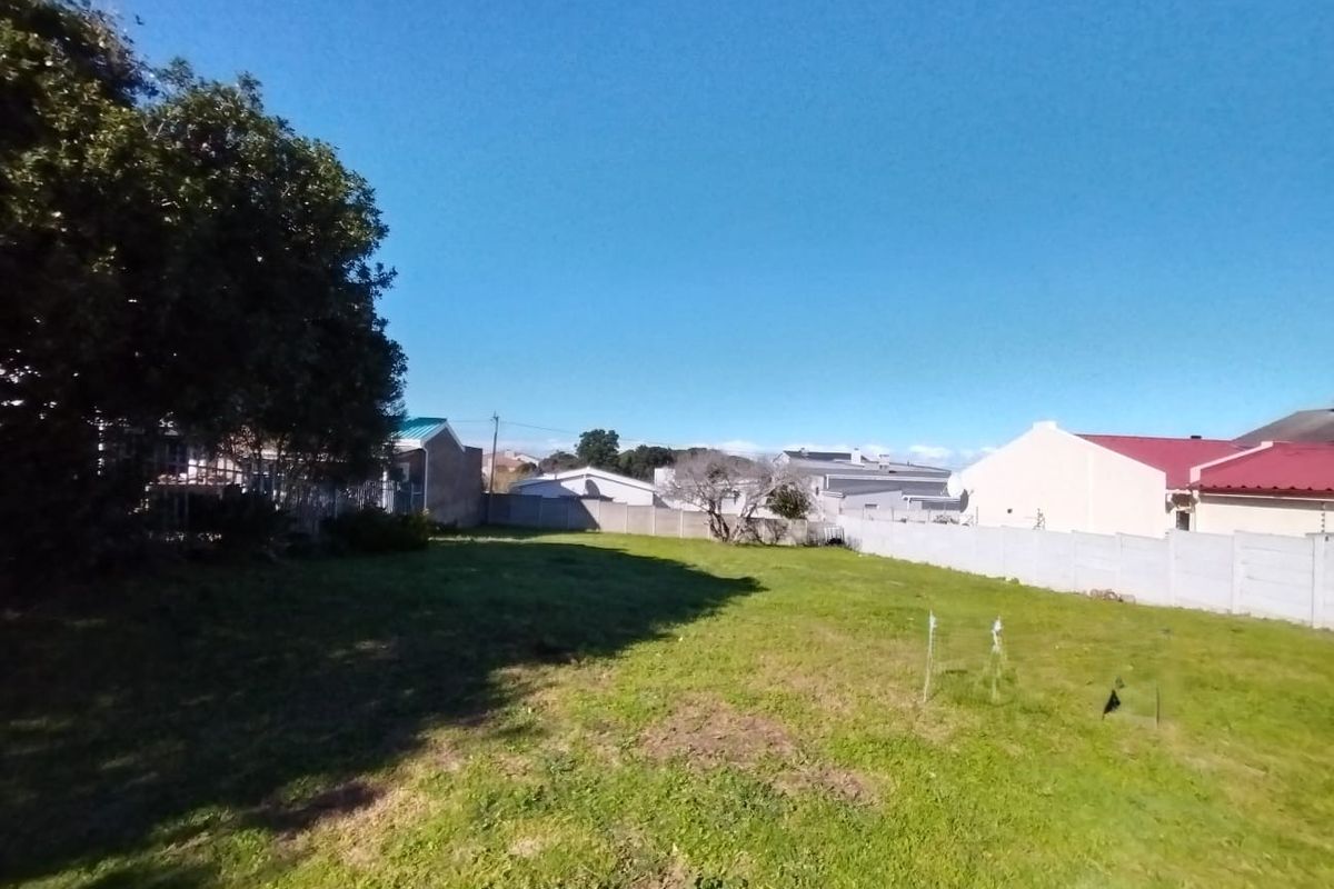 A vacant residential plot featuring a level grassed area enclosed by precast concrete boundary walls and mature trees.