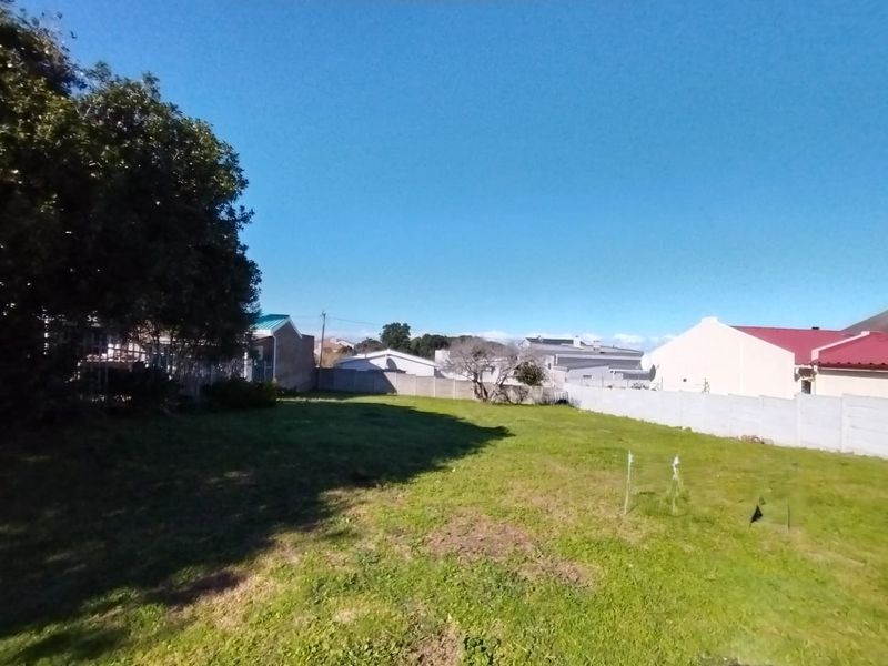 A vacant residential plot featuring a level grassed area enclosed by precast concrete boundary walls and mature trees.