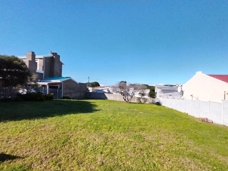 A vacant residential plot featuring a grassed area enclosed by precast concrete boundary walls and metal security fencing.