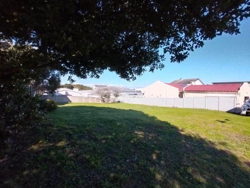 A spacious, level residential plot featuring a grassed lawn, mature tree, and secure precast concrete boundary walling.
