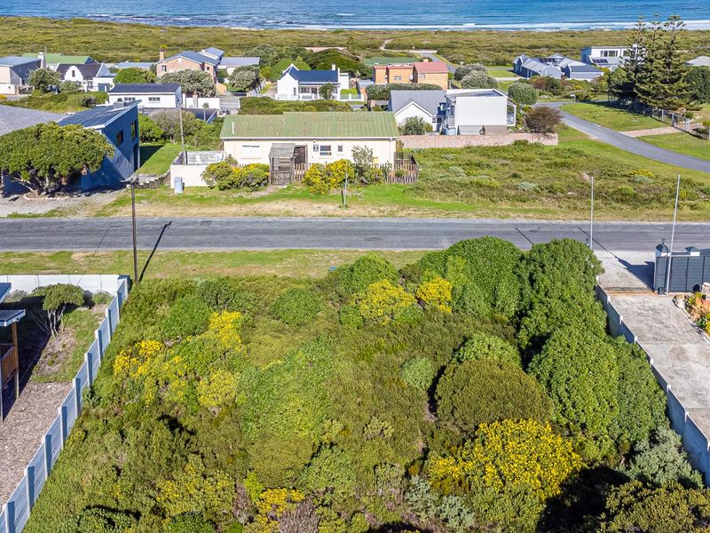 Aerial view of a vacant residential plot featuring coastal vegetation, situated in a developed neighborhood near the ocean.