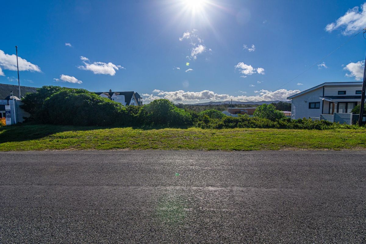A street-level view of the vacant residential land, showing the asphalt road frontage and surrounding landscape.