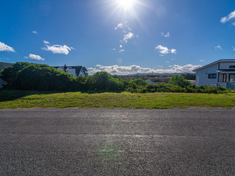 A street-level view of the vacant residential land, showing the asphalt road frontage and surrounding landscape.