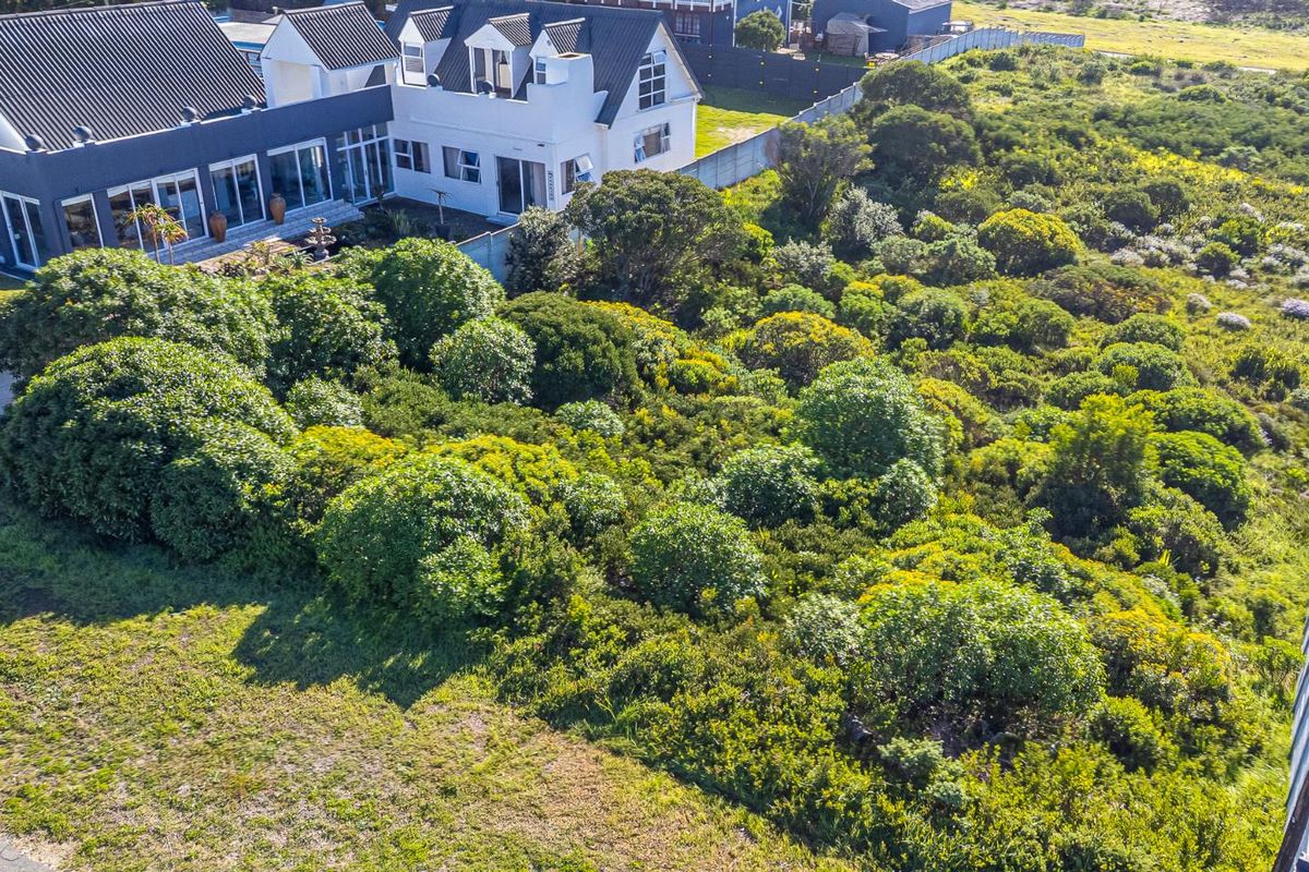 An aerial view of a vacant residential plot featuring dense native vegetation, perimeter fencing, and proximity to an existing residential property.
