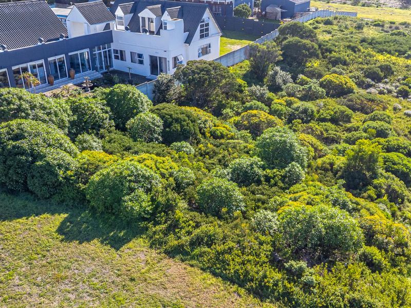 An aerial view of a vacant residential plot featuring dense native vegetation, perimeter fencing, and proximity to an existing residential property.