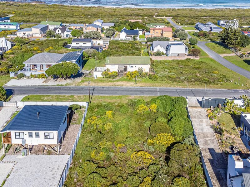Aerial view of a vacant residential plot featuring established vegetation, a concrete driveway, and boundary fencing in a coastal neighborhood setting.
