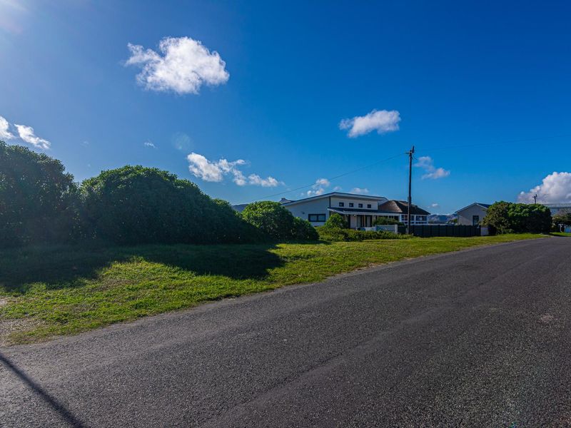 A street-level view of the vacant residential land, featuring an asphalt road frontage, grass verge, and established surrounding neighborhood infrastructure.