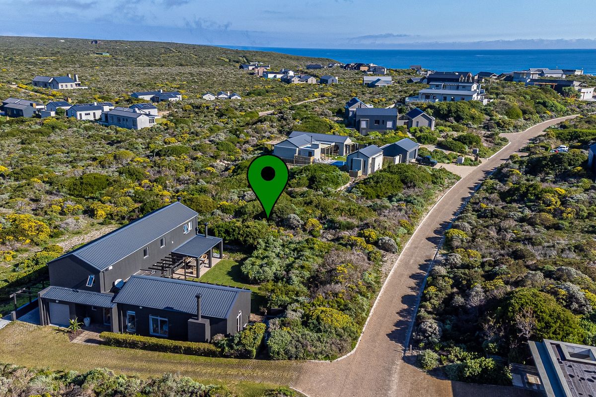 An aerial view of a vacant residential plot situated within a coastal estate, surrounded by natural fynbos vegetation and established modern homes.