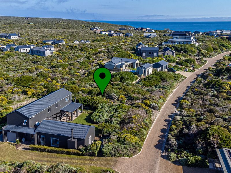 An aerial view of a vacant residential plot situated within a coastal estate, surrounded by natural fynbos vegetation and established modern homes.