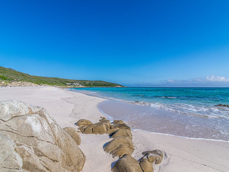 A scenic view of a pristine white sand beach with turquoise ocean waters and natural rock formations along the coastline.