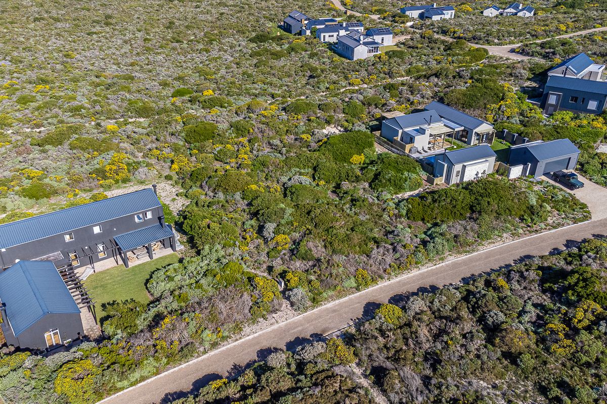 An aerial view of a residential estate featuring modern homes with metal roofs set within a natural fynbos landscape and gravel access roads.