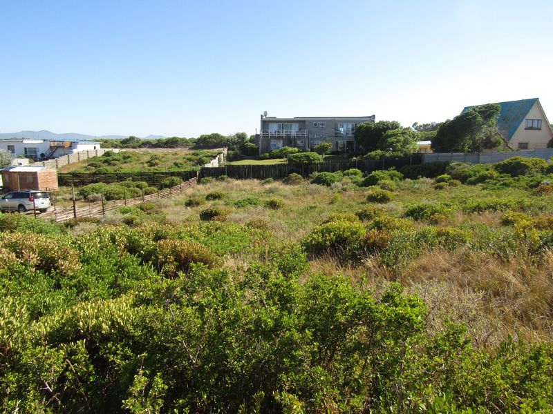 A vacant residential plot featuring natural coastal vegetation and perimeter fencing, situated in a developed neighborhood setting.
