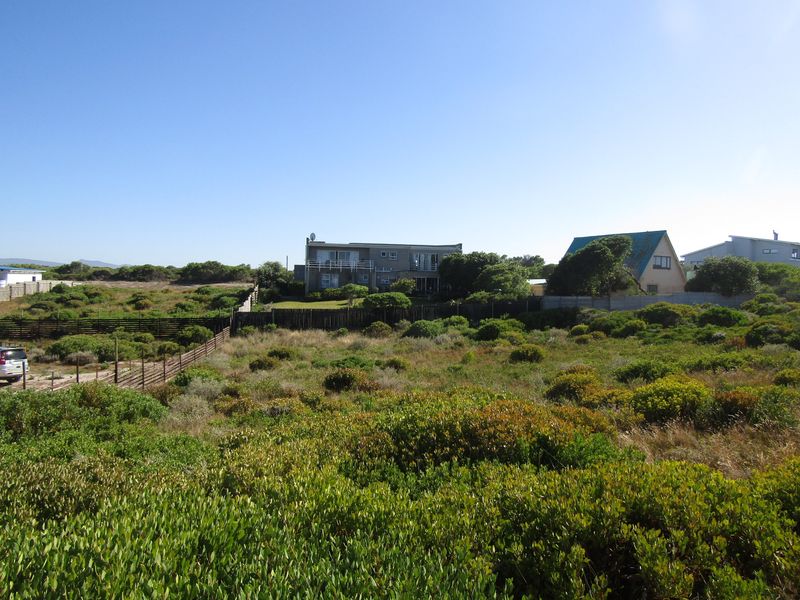 A view of a vacant residential plot featuring native coastal vegetation and perimeter fencing, with neighboring properties visible in the background.