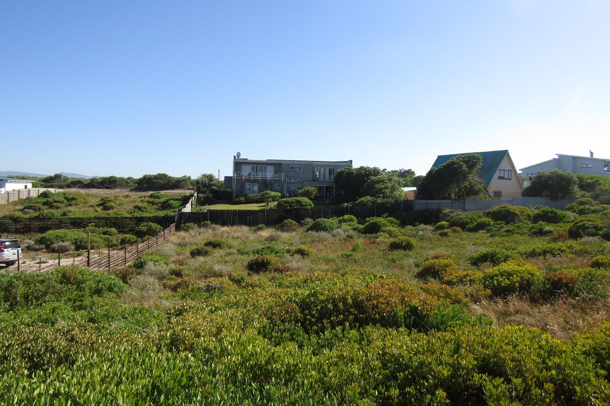 A view of a vacant residential plot featuring native coastal vegetation and perimeter fencing, with neighboring properties visible in the background.