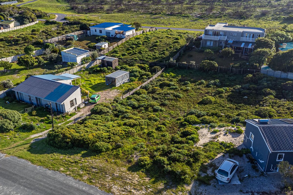 An aerial view of a residential vacant land plot featuring natural vegetation, perimeter fencing, and access to a gravel road.