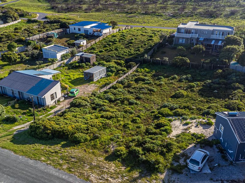 An aerial view of a residential vacant land plot featuring natural vegetation, perimeter fencing, and access to a gravel road.