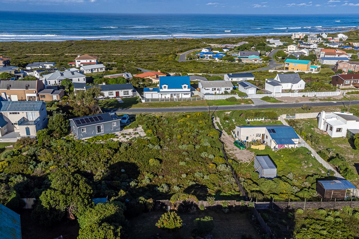 Aerial view of a vacant residential plot situated in a coastal neighborhood, featuring native vegetation and proximity to the ocean.