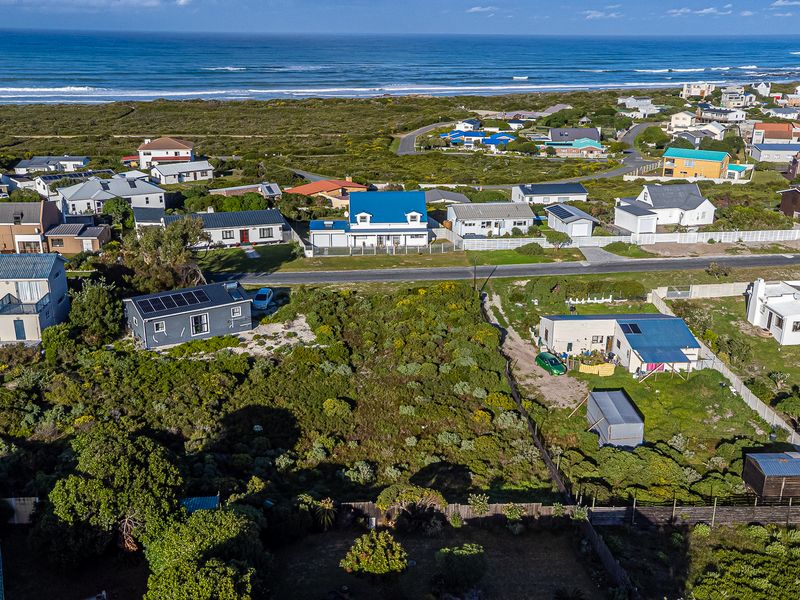 Aerial view of a vacant residential plot situated in a coastal neighborhood, featuring native vegetation and proximity to the ocean.