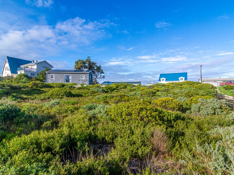 A wide-angle view of a residential plot featuring natural coastal vegetation and surrounding neighboring properties.