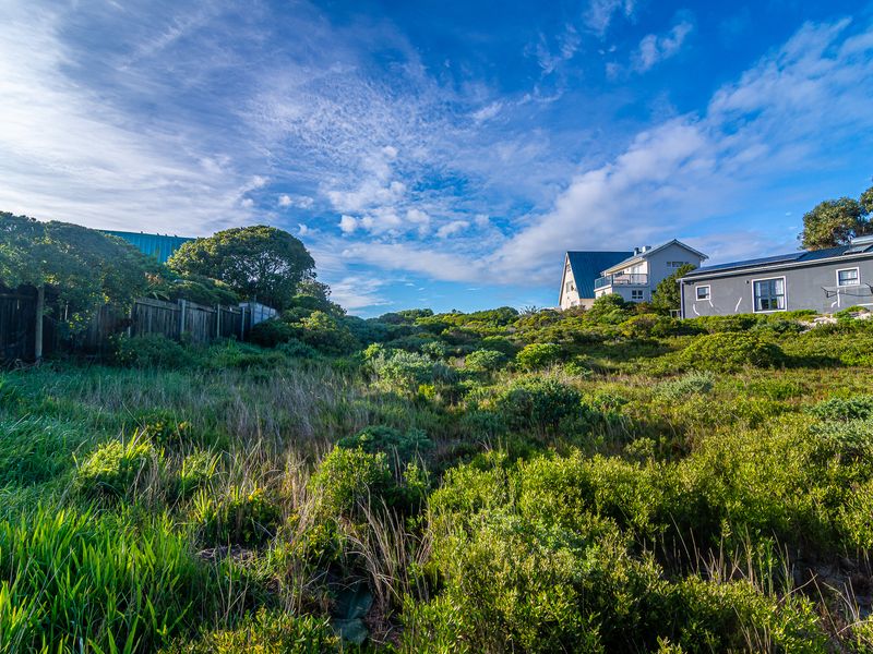 A view of a vacant residential plot featuring natural vegetation and perimeter fencing, with neighboring properties visible in the background.