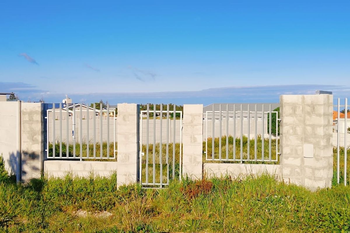 A vacant residential plot featuring a partially completed concrete block boundary wall with integrated metal palisade fencing and a pedestrian gate.