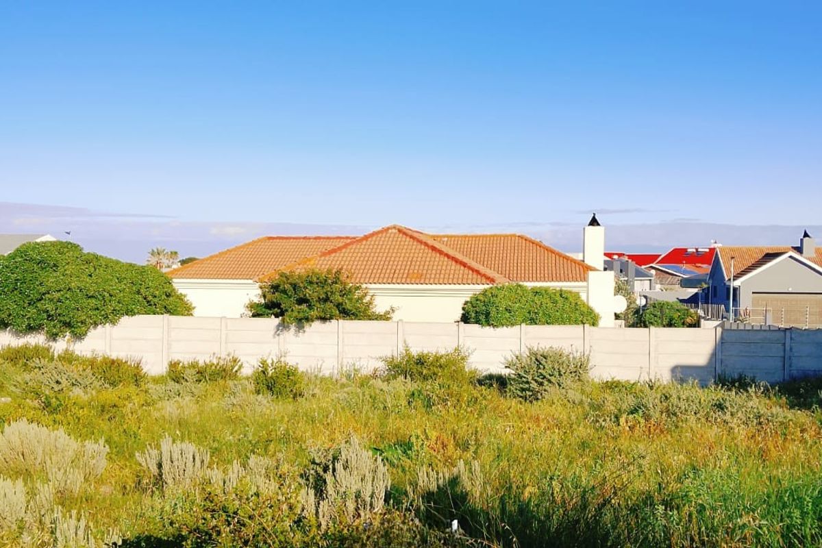 A view of a vacant residential plot featuring a precast concrete boundary wall with surrounding established residential properties in the background.