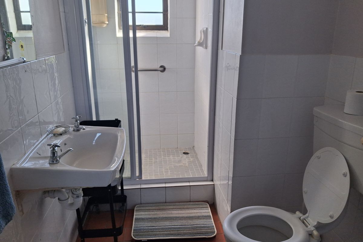 A functional bathroom featuring a shower enclosure, wall-mounted basin, and toilet with classic white wall tiling.
