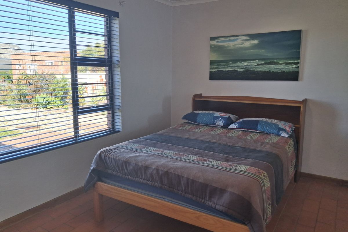 A bedroom featuring terracotta tile flooring and large windows with venetian blinds, offering natural light and a view of the exterior.