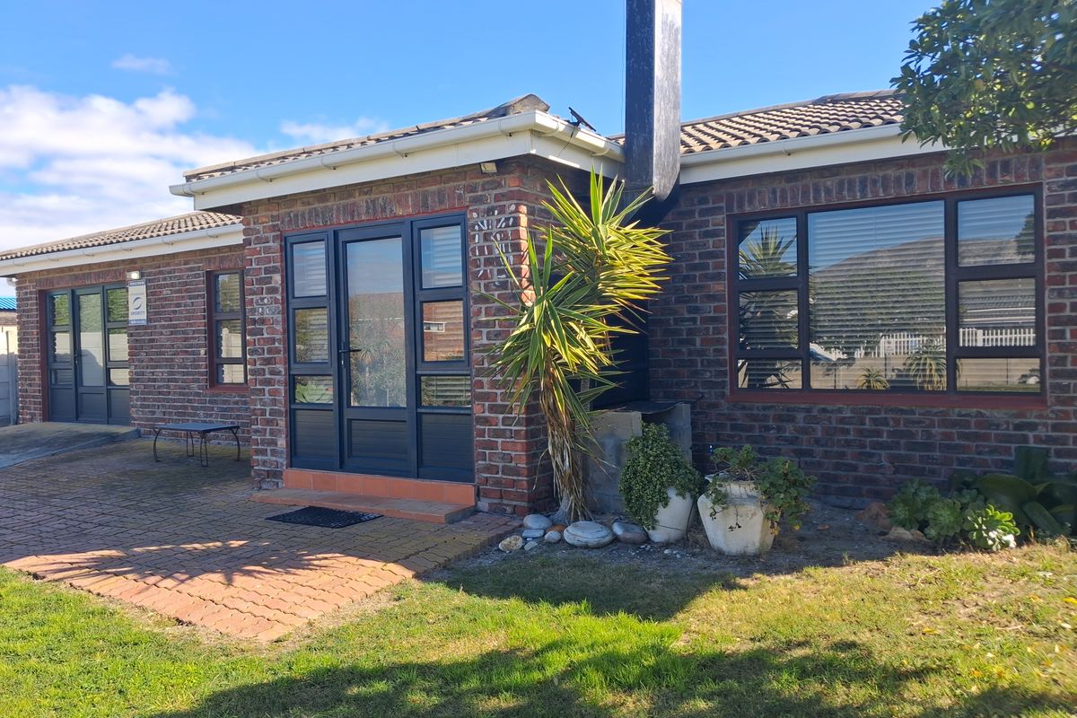 Rear exterior view of a brick house featuring a paved patio area, external chimney, and modern aluminium framed glass doors and windows.