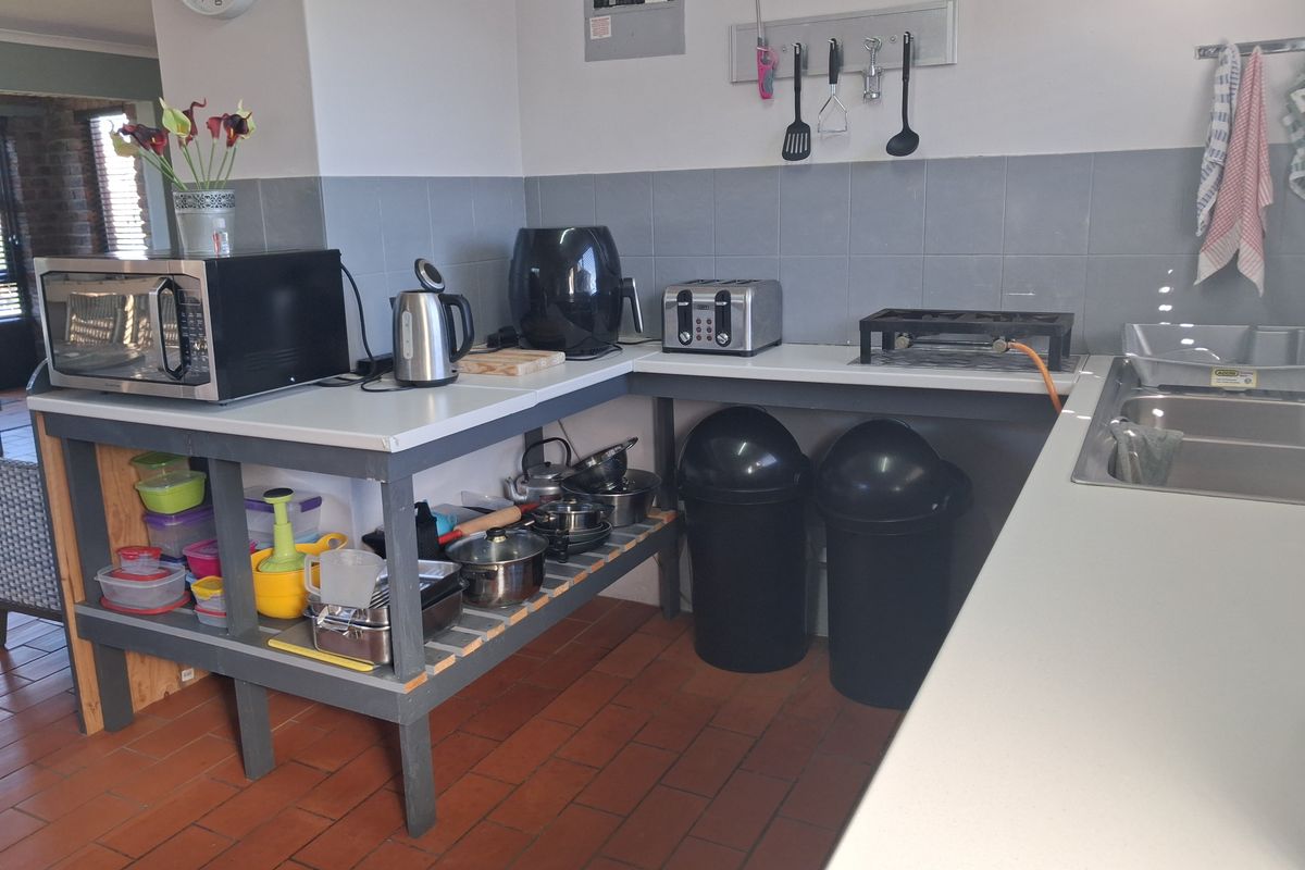 A functional kitchen area featuring a double stainless steel sink, tiled splashback, and terracotta flooring, currently utilizing open timber shelving for storage.