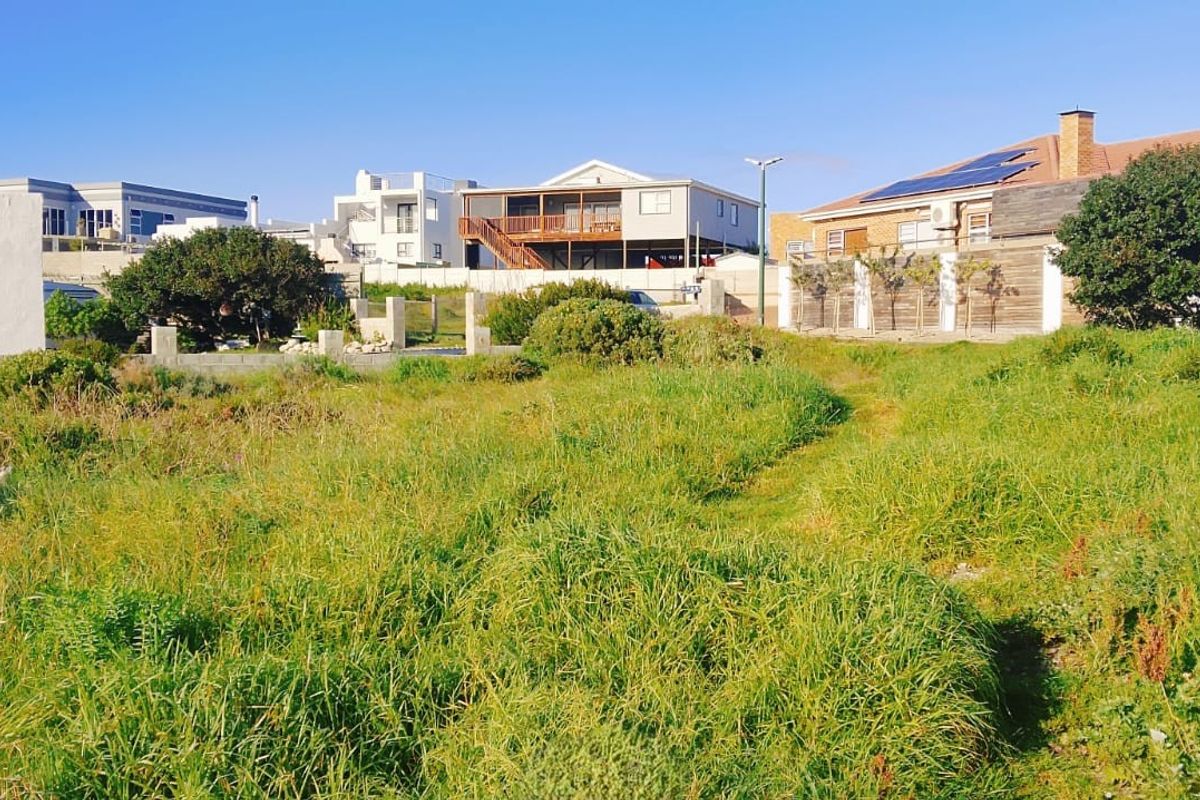 A vacant residential plot featuring natural grass coverage, surrounded by established neighboring properties and boundary fencing.
