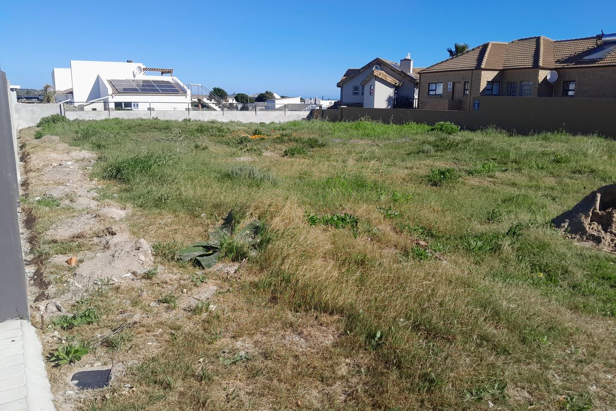A vacant residential plot of land featuring boundary walls and natural grass coverage, situated in a developed neighborhood.