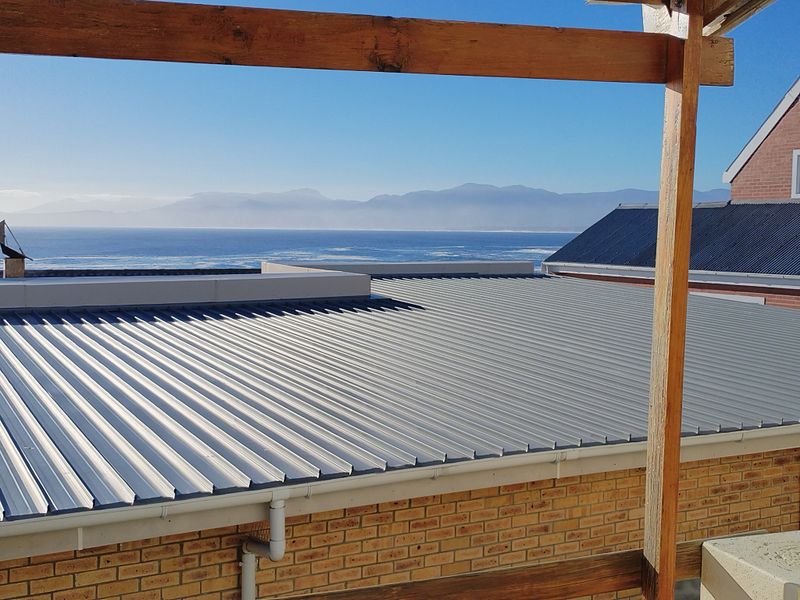 Elevated view overlooking a corrugated metal roof with a coastal and mountain backdrop.