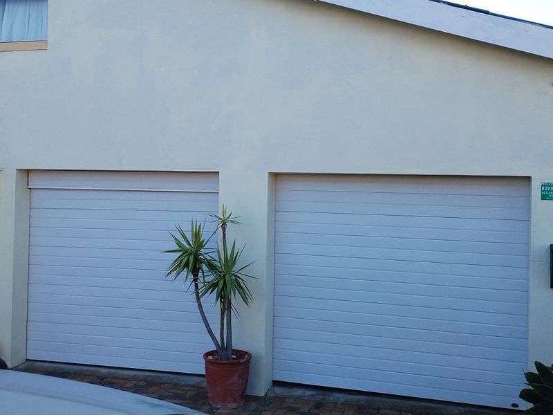 A view of a double garage with sectional doors and paved driveway access.
