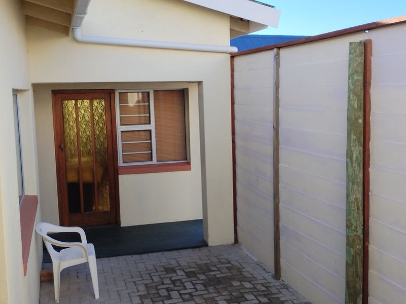 A paved outdoor patio area featuring a timber door, aluminium window, and a private boundary wall.