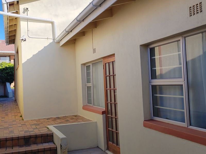 Rear exterior view of the property featuring brick paved steps, security-fitted windows, and a timber-framed door.