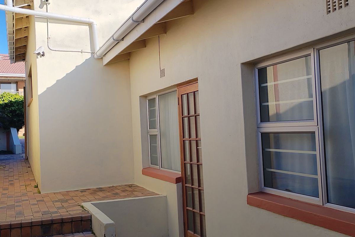 Rear exterior view of the property featuring brick paved steps, security-fitted windows, and a timber-framed door.