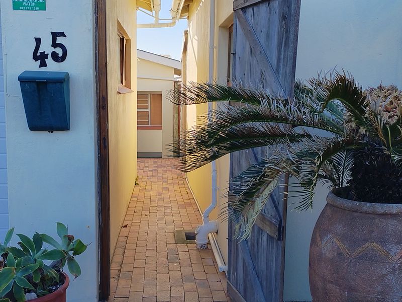 A narrow paved side walkway leading between two building structures, featuring a mailbox and house number on the exterior wall.