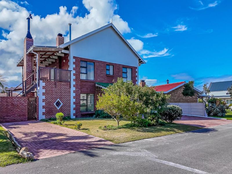 A well-maintained double-story brick house featuring a paved driveway, front lawn, and an elevated balcony with an external timber staircase.