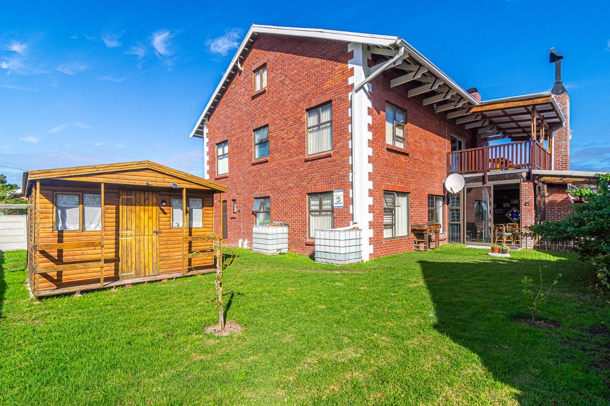 Rear view of a multi-story brick house featuring a wooden balcony, outdoor fireplace, and a detached timber garden shed set in a grassy yard.