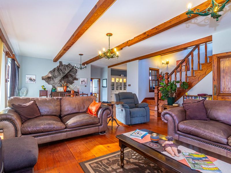Spacious living room featuring exposed timber ceiling beams, warm timber flooring, and a classic wooden staircase leading to the upper level.