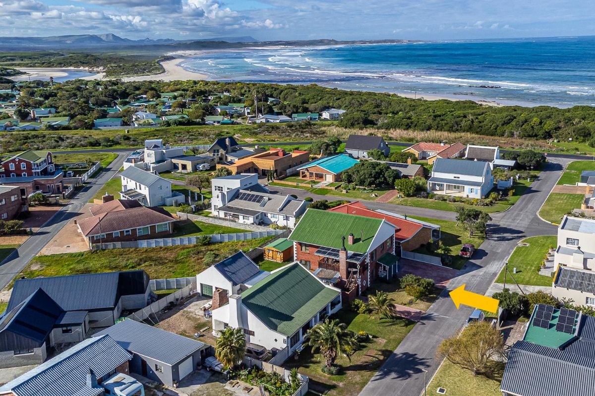 Aerial view of a coastal residential property featuring a pitched roof, solar panels, and a paved driveway, situated near the beach.