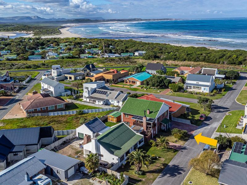 Aerial view of a coastal residential property featuring a pitched roof, solar panels, and a paved driveway, situated near the beach.