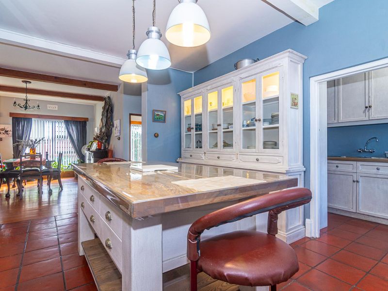 A spacious kitchen featuring a large central island, built-in display cabinetry, terracotta flooring, and exposed timber beams, with an adjacent scullery area.