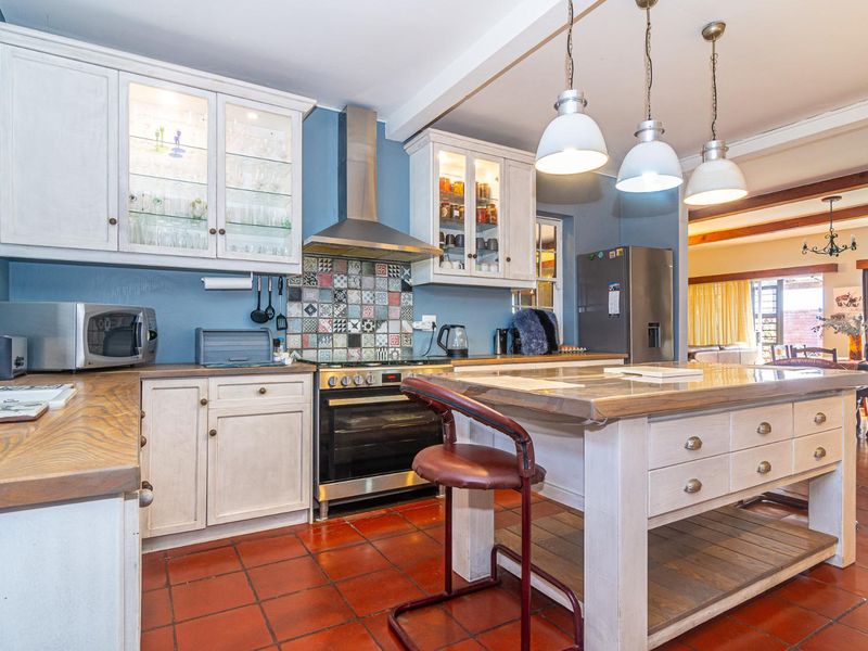 A well-appointed kitchen featuring a central island, built-in cabinetry, stainless steel appliances, and a decorative tiled backsplash, finished with terracotta flooring.